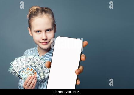 Heureuse jeune femme tient smartphone avec écran blanc vide blanc et argent cash US dollars sur fond bleu Banque D'Images