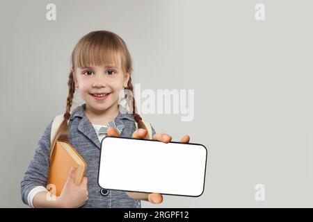 Joli enfant élève d'école souriant avec écran blanc vide vierge sur smartphone. Bannière de maquette pour nouvelle application, éducation ou websit mobile Banque D'Images