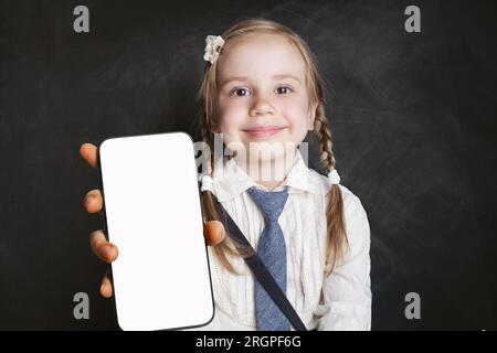 Mignon jeune fille élève de l'école tenant smartphone avec l'affichage blanc vide vide d'écran. Bannière de maquette pour nouvelle application, éducation ou websit mobile Banque D'Images