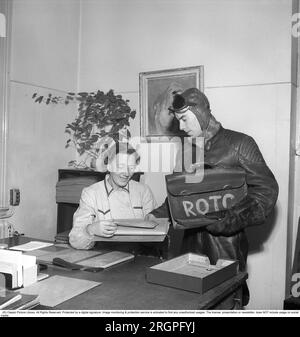 Sven-Eric Gamble. 1924-1976. Acteur suédois. Il devait souvent incarner des méchants au cinéma et sur scène. Photographié ici à droite pendant qu'il travaillait comme messager pour l'imprimerie Nordisk Rotogravyr et livrait et ramassait en leur nom. Il conduisait une moto et les vêtements étaient la veste en cuir typique avec des épaulettes. Au lieu d'un casque, ils portaient une capuche en cuir et des lunettes. On le voit ici avec une dame dans un bureau avec des colis à livrer ou à recevoir. Suède 1953. Kristoffersson réf. BM72-10 Banque D'Images