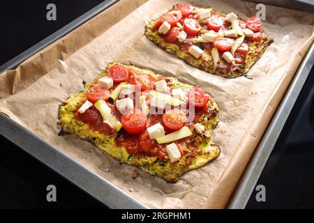 Morceaux de pizza végétariens sur une croûte de courgettes et flocons d'avoine, garnis de tomates et de fromage feta sur un plateau avec du papier sulfurisé, sain faible carb me Banque D'Images