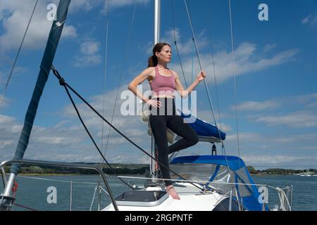 Femme sportive appuyée contre le mât d'un bateau au soleil. La vie de yachting. Banque D'Images