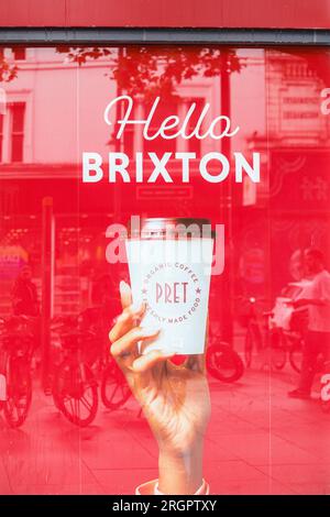 Bonjour Brixton, PRET a manger café publicité de fenêtre avec la main tenant le café et slogan, les gens reflétés dans la fenêtre, Brixton, Londres, Angleterre, Royaume-Uni Banque D'Images