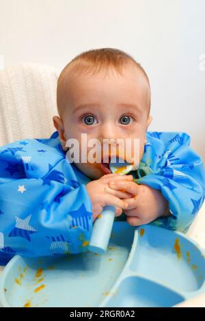 Bébé aux yeux bleus mangeant de la soupe par lui-même avec une cuillère en silicone Banque D'Images