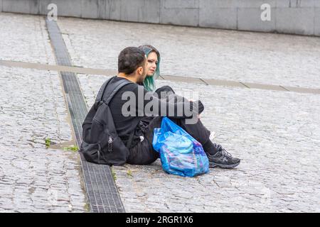 Jeune couple assis sur la place pavée parlant ensemble - Paris, France. Banque D'Images