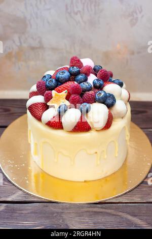 Gâteau d'anniversaire jaune avec des fraises trempées dans du chocolat blanc, des framboises fraîches et des myrtilles sur fond vintage Banque D'Images