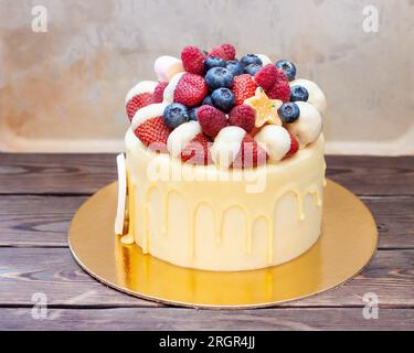 Gâteau d'anniversaire jaune avec des fraises trempées dans du chocolat blanc, des framboises fraîches et des myrtilles sur fond vintage Banque D'Images