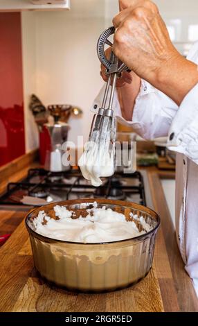 Femme cuisinier à la maison fouettant les blancs d'œufs à des pics raides à la main pour faire une mousse au chocolat ou meringue Banque D'Images