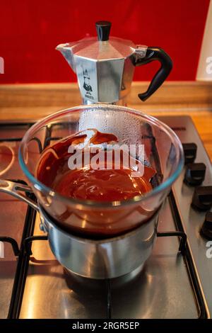 Faire fondre le chocolat noir dans un bol en verre au-dessus d'une casserole chaude sur une plaque de cuisson à gaz dans la cuisine Banque D'Images