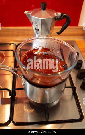 Faire fondre le chocolat noir dans un bol en verre au-dessus d'une casserole chaude sur une plaque de cuisson à gaz dans la cuisine Banque D'Images