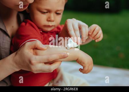 Mère met de la crème sur la main de bébé en été Banque D'Images