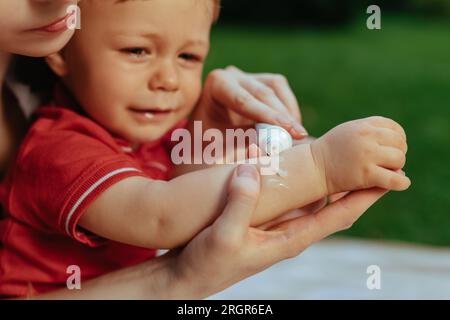 Mère met de la crème sur la main de bébé en été Banque D'Images