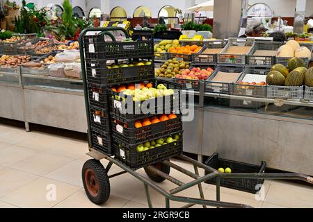 Chariot avec des boîtes de fruits pour réapprovisionner les présentoirs à l'intérieur du marché local Mercado Coletivo Aveiro avec des stands vendant des fruits frais, des légumes, Portugal Banque D'Images