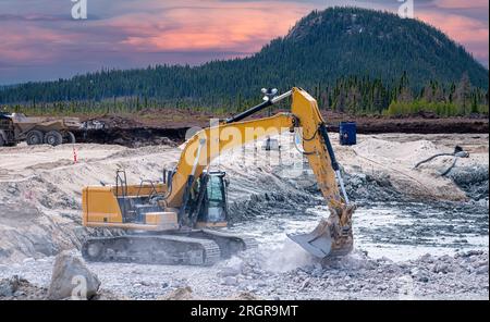 Excavatrice jaune travaillant sur un chantier dans la taïga au coucher du soleil Banque D'Images