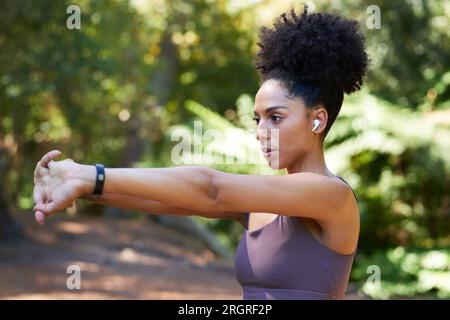 Femme multi-ethnique sérieuse étire les bras avant de courir sur sentier dans la forêt, l'exercice Banque D'Images