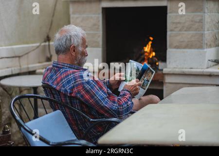 Un vieil homme dans une chemise à carreaux à la maison est assis à une table et lit le journal. Un homme âgé fermier et pêcheur repose dans sa propre villa. Banque D'Images