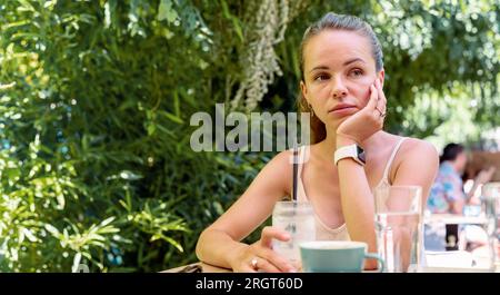 Triste femme urbaine fatiguée assise à la table dans un café en été, maladie mentale, apathie, solitude. Banque D'Images