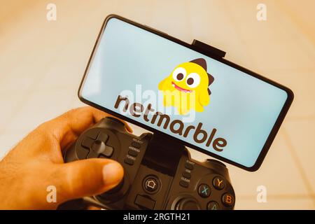 Dans cette illustration photo, une personne joue sur un joystick et le logo Netmarble s'affiche sur l'écran d'un smartphone. Banque D'Images