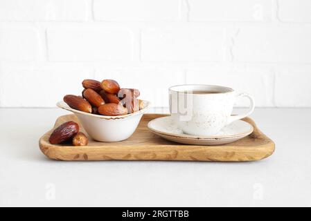 Thé et dattes dans un plateau en bois Dattes séchées sur fond blanc. Bonbons naturels. Nourriture pour Ramadan. Banque D'Images