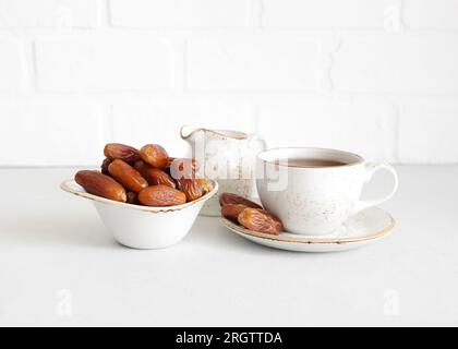 Thé et dattes séchées dans un bol sur fond blanc. Bonbons turcs. Nourriture saine naturelle. Banque D'Images