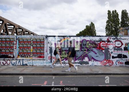 Des gens sont vus marcher près d'un mur repeint par le conseil de Tower Hamlets mais toujours avec des slogans anti-gouvernement chinois dans Brick Lane. Le 5 août, les étudiants du Royal College of Arts (RCA) ont peint le mur en blanc et recouvert tous les graffitis existants des 12 valeurs fondamentales du socialisme pendant la Révolution culturelle, déclenchant un débat animé entre les artistes locaux et les communautés chinoises et remettant en question la propagation de la propagande pro-chinoise. Depuis le 8 août, le Conseil de Tower Hamlets a publié une déclaration exhortant les gens à cesser de peindre encore plus de graffitis illégaux sur le mur Banque D'Images