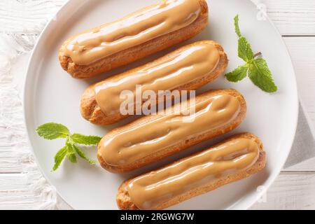 Eclaires sucrés français garnis de crème et garnis de caramel délicat doux gros plan dans une assiette sur la table. Vue de dessus horizontale Banque D'Images