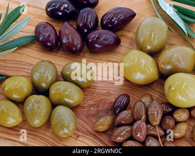 Gros plan de différents types d'olives sur une assiette de service en bois, des olives mélangées de différentes tailles comme un apéritif sain Banque D'Images