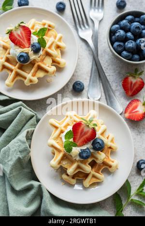 Gaufres fraîchement cuites avec fraises et myrtilles sur un fond gris béton. Cuisson maison. Banque D'Images