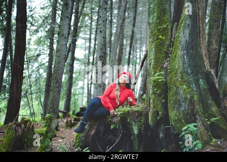 Femme avec une attitude positive sur une souche d'arbre mousseline au milieu de la forêt. Banque D'Images