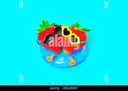 Joie rafraîchissante de l'été : vue de haut en bas d'un duo de fraises, enfilant des lunettes de soleil tendance, flottant sur une flottaison gonflable vibrante. Journées ensoleillées, cool wat Banque D'Images