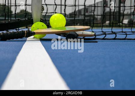 Ramettes de Pickleball et deux boules jaunes de fouet sur un court bleu sur une ligne blanche en gros plan. Banque D'Images