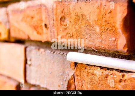 Craie blanche d'école coincée dans un mur vétuste de briques rouges endommagées. Banque D'Images