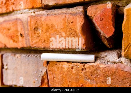 Craie blanche d'école coincée dans un mur vétuste de briques rouges endommagées. Banque D'Images