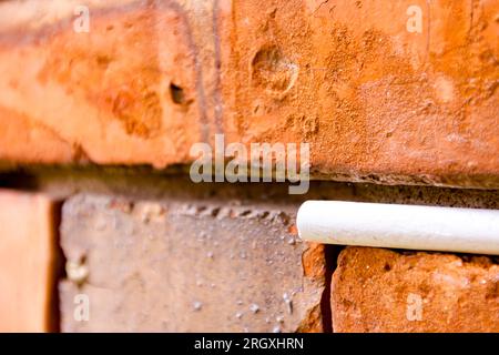 Craie blanche d'école coincée dans un mur vétuste de briques rouges endommagées. Banque D'Images