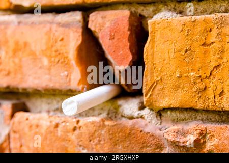 Craie blanche d'école coincée dans un mur vétuste de briques rouges endommagées. Banque D'Images