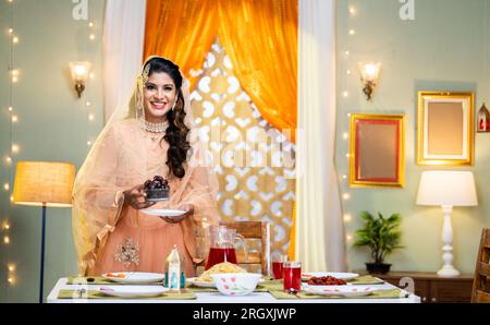 Portrait de femme indienne souriante heureuse avec des dates en main regardant la caméra à la maison - concept de fête du ramadan, tradition et plaisir. Banque D'Images