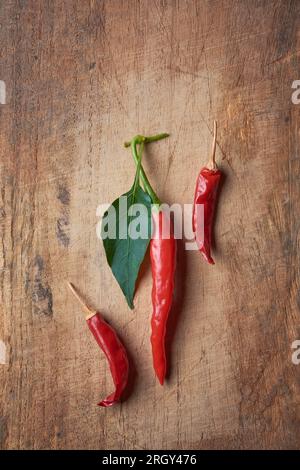 piment rouge, aka piments chili ou piments forts avec des feuilles sur fond de table en bois, épice populaire utilisée dans les cuisines du monde entier, pris droit Banque D'Images