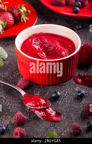 Sorbet aux baies. Dessert rafraîchissant d'été de diverses baies : framboise, myrtille, fraise dans de la vaisselle rouge sur fond sombre Banque D'Images