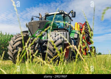 Paysage agricole créatif. Vue à faible angle à travers l'herbe jusqu'au tracteur avec semoir. Banque D'Images