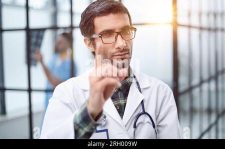 médecin attentif dans un manteau blanc pointant son doigt vers vous tout en se tenant dans le couloir de l'hôpital Banque D'Images