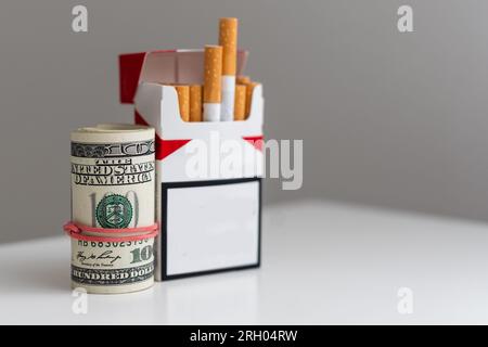 Paquet de cigarettes sur une photo de billets de cent dollars. Concept de coût élevé du tabagisme Banque D'Images