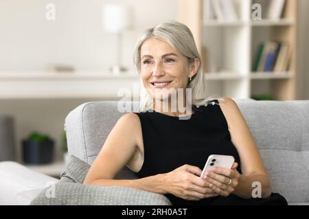 Heureuse femme d'âge moyen rêveuse tenant smartphone Banque D'Images