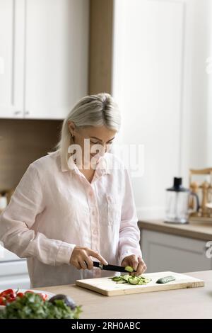 Femme au foyer mature positive cuisinant le dîner maison dans la cuisine à la maison Banque D'Images