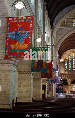 intérieur d'une cathédrale gothique renaissance, avec des bannières colorées semées à la main représentant des scènes religieuses suspendues au-dessus des bancs avec des vitraux Banque D'Images