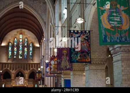 intérieur d'une cathédrale gothique renaissance, avec des bannières colorées semées à la main représentant des scènes religieuses suspendues au-dessus des bancs avec des vitraux Banque D'Images