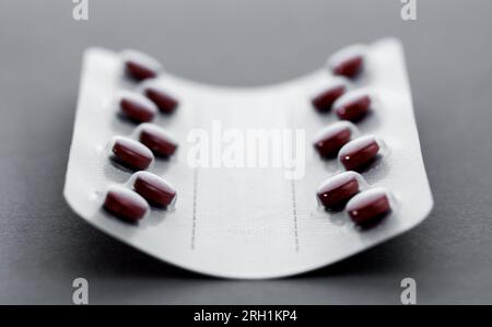 Emballage en feuille pour comprimés. Les pilules rouges dans un blister reposent sur une table sombre. Concept de pharmacie. Banque D'Images