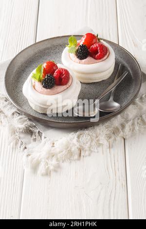 Pavlova meringue nid avec des baies et des feuilles de menthe sur une assiette sur la table en bois. Vertical Banque D'Images