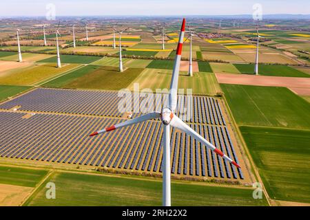 Vue rapprochée aérienne d’une éolienne devant des champs agricoles et des panneaux photovoltaïques d’un parc solaire en crise énergétique Banque D'Images