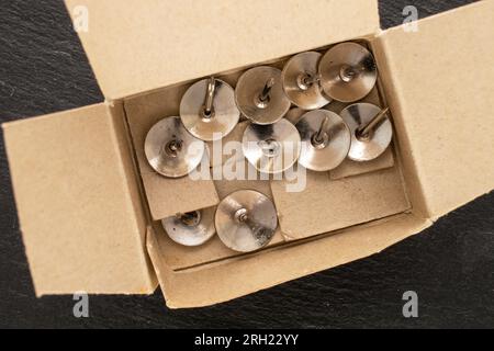 Plusieurs boutons métalliques dans une boîte en papier sur pierre d'ardoise, macro, vue de dessus. Banque D'Images
