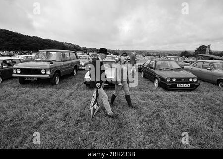 Homme et femme propriétaires de voitures anciennes en parures chapeau melon parapluie et vestes marchant parmi les voitures classiques Carnhell Green Vintage Rally 12 août 2023 Banque D'Images